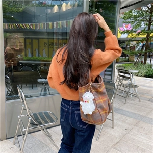 Back view of a woman wearing an orange sweater carrying a plaid wool tote bag outdoors
