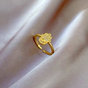 Macro view of gold Hamsa hand ring with white crystals on purple satin fabric