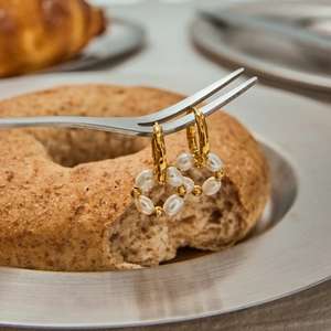 Gros plan de boucles d'oreilles créoles dorées avec perles sur une fourchette pour le détail