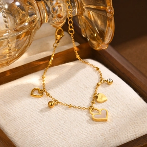 Detailed close-up of a gold heart charm bracelet with pearl accents and Love engraving