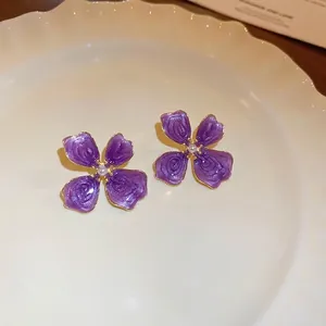 Violet enamel flower stud earrings with rose texture and pearl center on white plate
