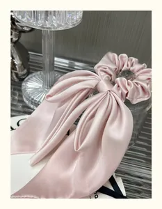Elegant pale pink satin bow hair scrunchie with long ribbons on a decorative glass background