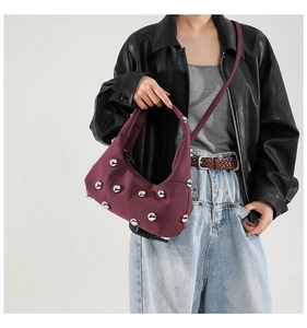Detail of burgundy crossbody bag with large silver rivets and half-moon canvas structure