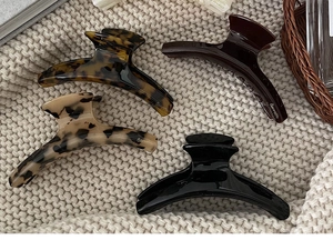 Flat lay of acetate claw clips in four colors on a beige knitted blanket background