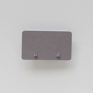 Macro view of dainty light purple zircon stud earrings in silver prong setting on card