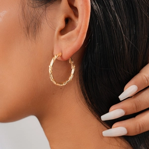 Detail of a textured golden twist hoop earring worn by a model in a clean studio setting
