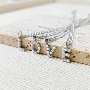 Detail of silver letter L O V E pendants with pearl inlay on minimalist necklaces