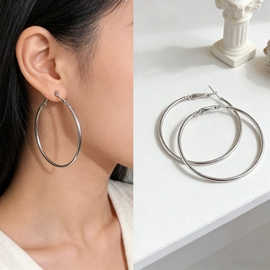 Detail view of large silver hoop earrings worn by a model and displayed on a white stand
