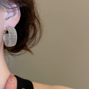 Macro shot of silver-tone C-shape hoop earrings with a textured mesh woven pattern on model