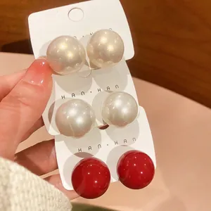 Three pairs of elegant round pearl stud earrings in white, champagne, and vibrant red
