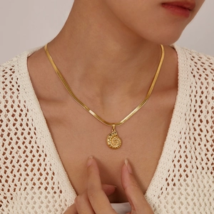 Detail of gold conch shell pendant on a flat snake chain necklace worn by a model