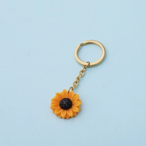 Detail of yellow sunflower keychain with golden metal ring on a light blue background