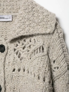 Detail of chunky knit cardigan featuring hollow-out texture and large black buttons