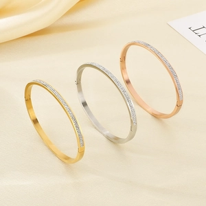 Tre bracciali ovali in acciaio placcati oro 18k con zirconi su sfondo di seta