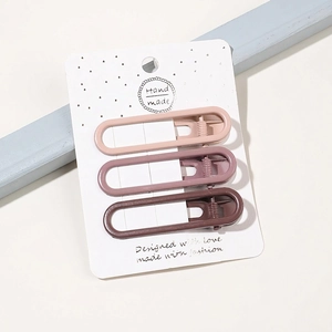 Detailed view of three brown and pink metal hair clips set on handmade paper card