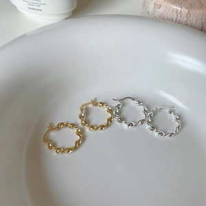 Macro view of gold and silver irregular twisted hoop earrings in a minimalist ceramic dish