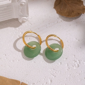 Close-up of gold hoop earrings with green stone donut pendants on white textured background