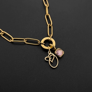 Detailed view of gold paperclip chain necklace with pink gem and script initial O charm.