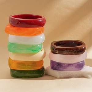 Stack of thick square resin bangles with marble and amber textures on white stone base