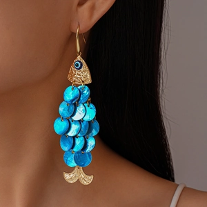 Close-up of a gold and blue shell fish-shaped drop earring on a model's ear