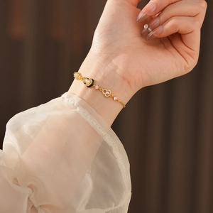 Detail of a gold-plated bracelet featuring white pearls and black enamel heart charms