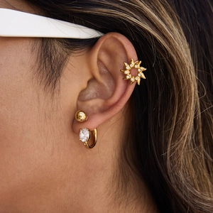 Close-up of gold sun-shaped ear cuff and oval cubic zirconia stud earrings set on ear