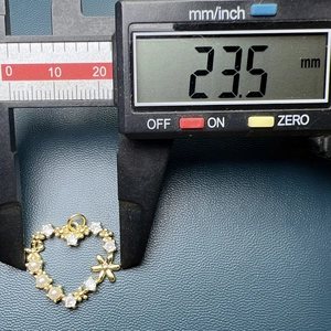 Digital caliper measuring the 23.5mm width of a golden heart pendant with pearls