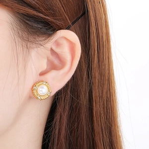 Close-up of a gold pearl stud earring with rhinestone halo worn on a woman's ear