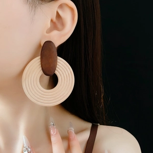Gros plan de grandes boucles d'oreilles bohèmes géométriques en bois portées sur fond noir
