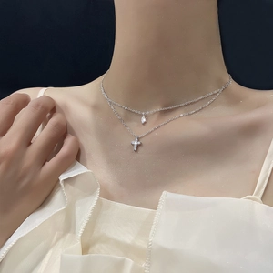Detailed view of silver layered necklace with zircon cross and water drop pendant on neck