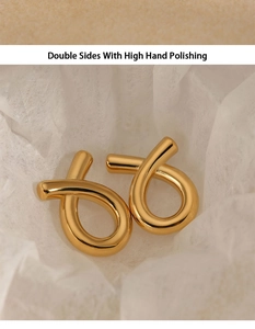 Detail of gold fish-style twisted earrings with high hand polished finish on white background
