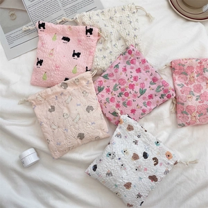 Flat lay of multiple cute cartoon drawstring storage bags on white fabric background