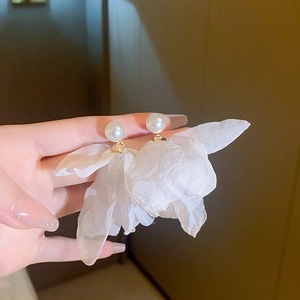 Close-up of white tulle flower earrings with pearls held between fingers for scale
