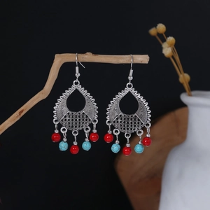 Bohemian silver drop earrings with red and blue beads hanging on a wooden branch