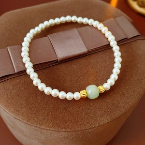 Detailed macro of vintage pearl bracelet with green jade bead on brown velvet background