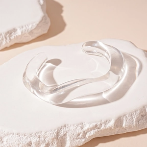 Detailed view of a transparent acrylic wavy open bangle on a natural white stone platform