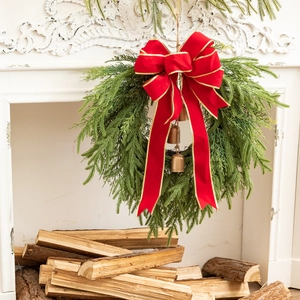 Detail of Christmas wreath with red velvet bow and vintage bells on a white fireplace