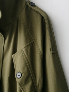 Detail of army green cotton trench coat showing epaulets and matte black buttons