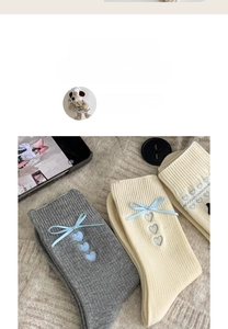 Details von grauen Socken mit blauen Seidenschleifen und gestickten Herzen auf weichem Teppich