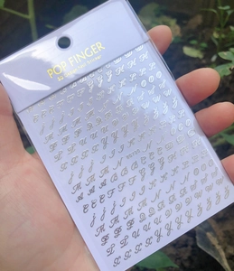 Detailed close-up of 3D gold cursive letter nail stickers style WG720 for manicure