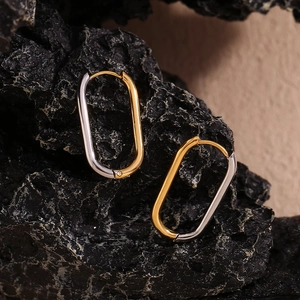 Macro detail of oval hoop earrings with gold-silver contrast and a small diamond accent