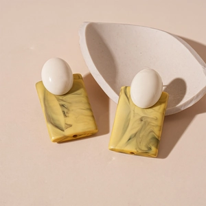 Vue détaillée de boucles d'oreilles rétro en acrylique blanc et pendentifs marbre jaune