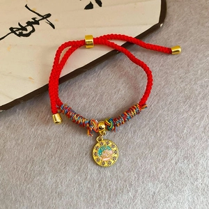 Vue détaillée du bracelet tressé rouge avec pendentif Fu doré et fils multicolores de soie