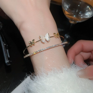 Detail of stacked gold bracelets featuring zircon butterflies and white shell inlay