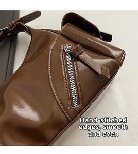 Detail of a brown glossy leather shoulder bag showing zipper and handmade stitching