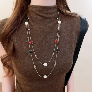 Détail du collier doré double couche avec perles en résine et verre sur un pull marron