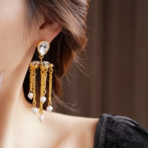 Close-up of golden vintage-style tassel earrings with crystals and small pearls on a model