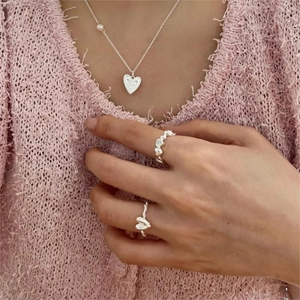 Detail of 925 sterling silver heart ring and pearl necklace on a soft pink background
