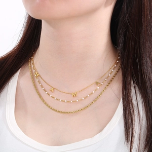 Detailed close-up of layered golden MAMA letter necklace with twisted rope and pearl beads