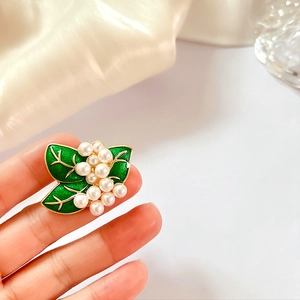 Detail of vintage flower brooch with green enamel leaves and white pearls held in hand
